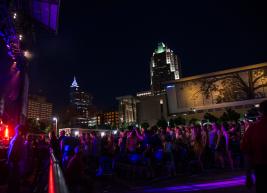Downtown Raleigh shimmers at night in the background of a band performing at Red Hat Amphitheater